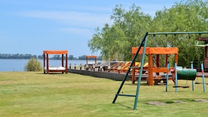 A playground with swings and a slide, a bench, and a view of a lake.