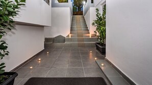 Una escalera moderna con vistas a árboles en la parte superior, rodeada de paredes blancas y plantas en macetas.