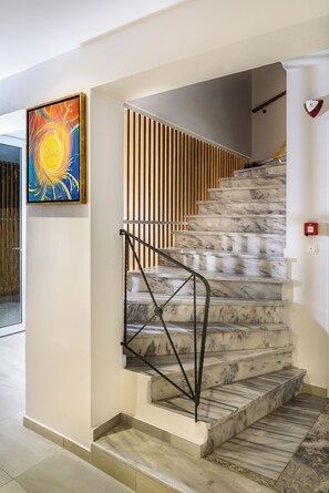 A marble staircase with black metal railings, a wooden slatted wall, and a colorful abstract painting on the wall.