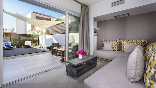 Una sala de estar moderna con un sofá, una mesa de centro y un ventanal corredera que da a un espacio exterior con patio y mobiliario.