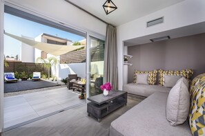 Ein modernes Wohnzimmer mit einer Couch, einem Couchtisch und einer Schiebetür zu einem Außenbereich mit Terrasse und Sitzgelegenheiten.