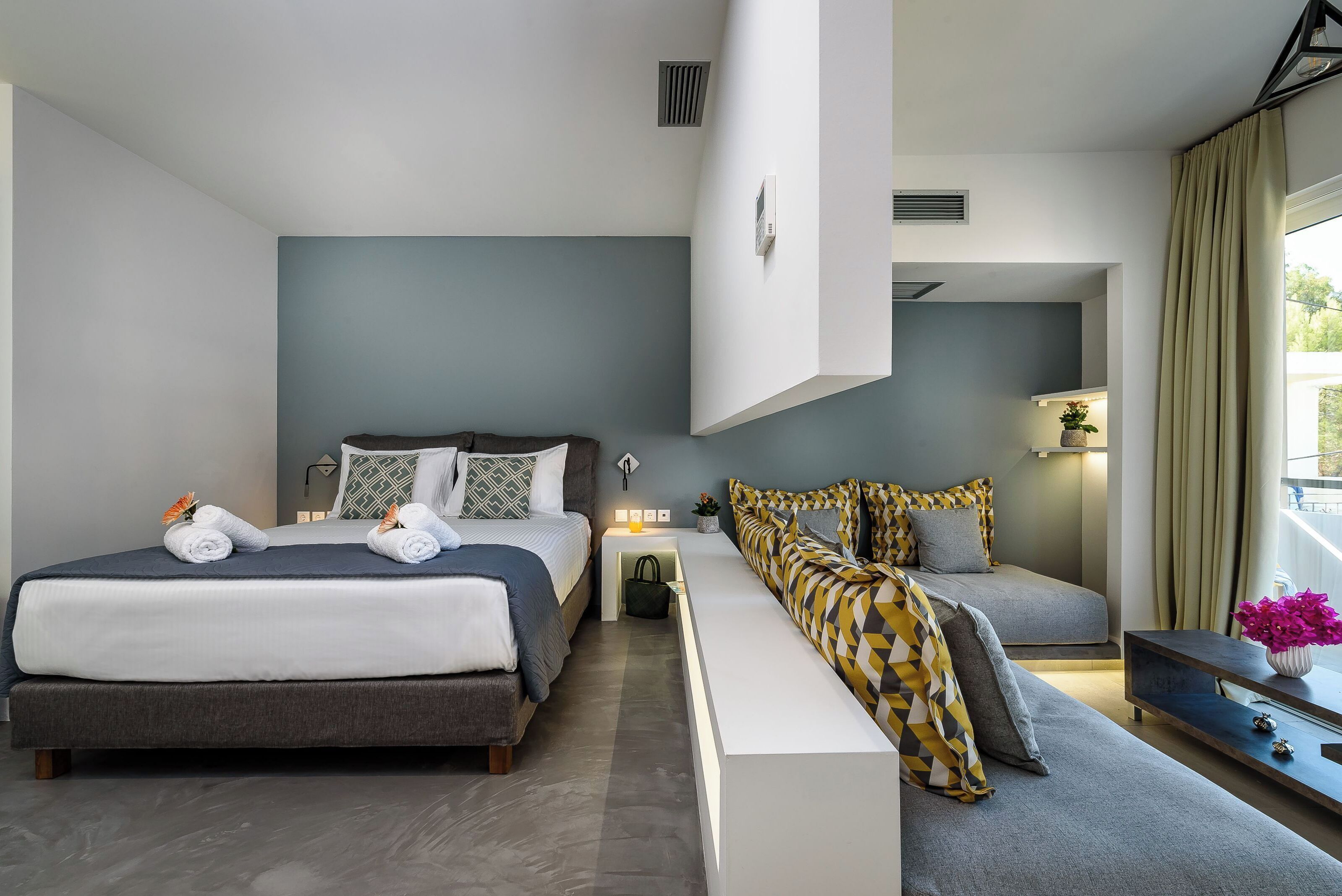 Ein modernes Hotelzimmer mit einem großen Bett, einem Sofa, einem kleinen Tisch und einem Fenster mit Vorhängen.
