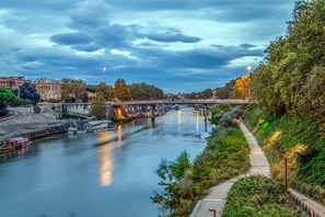 Un río con un puente, un camino a su lado y edificios al fondo.