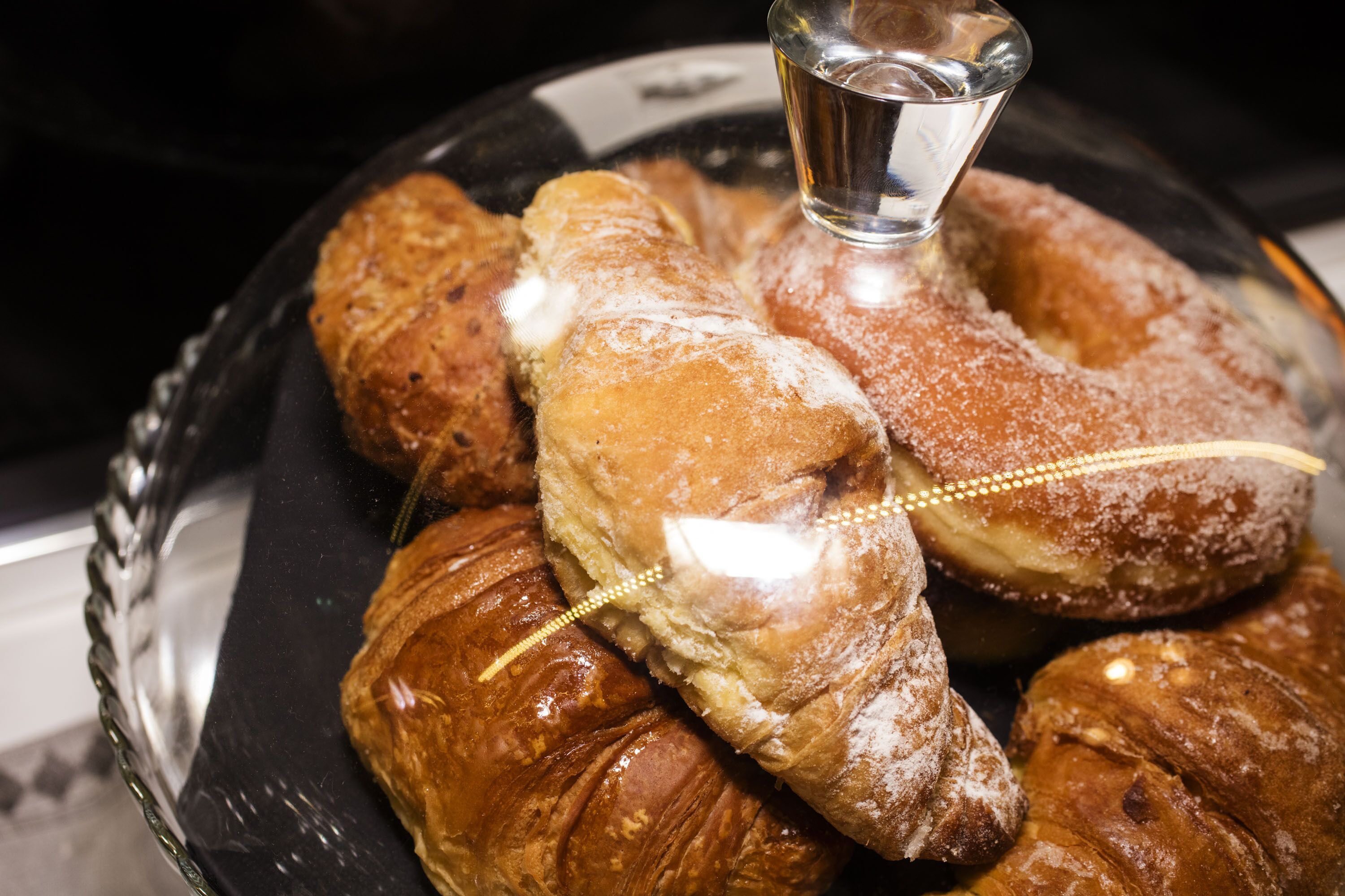 Un cuenco de vidrio con varios pasteles, incluyendo croissants y una rosquilla cubierta de glaseado.
