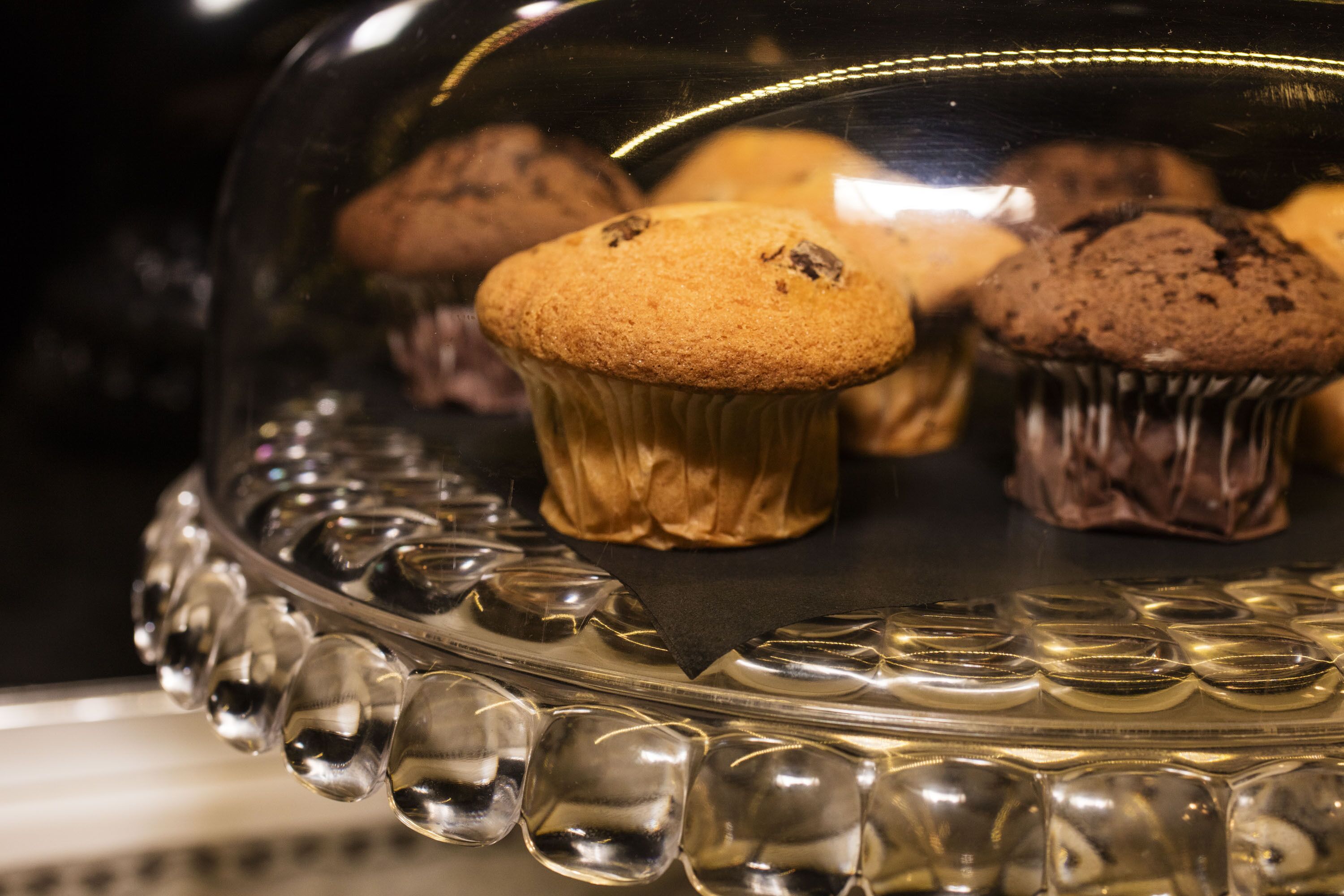 A glass display case with a decorative base, containing several muffins.