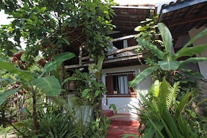 A two-story building with a red exterior and white walls, surrounded by lush greenery including banana trees and various tropical plants. - casa gaiolas (Ubatuba)