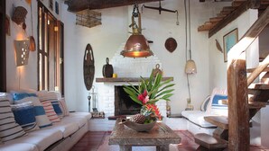 A cozy living room with a sofa, a wooden table with a fruit bowl, and a fireplace. - casa gaiolas (Ubatuba)