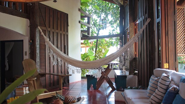 A hammock in a room with a wooden floor, a sofa, and a table with a bowl of fruit. - casa gaiolas (Ubatuba)