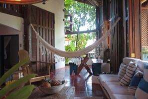 A hammock in a room with a wooden floor, a sofa, and a table with a bowl of fruit.