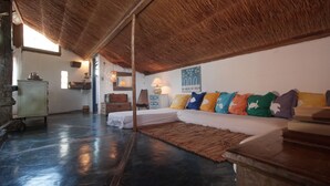A spacious room with a thatched roof, a large bed with colorful pillows, a wooden cabinet, and a stone fireplace. - casa gaiolas (Ubatuba)