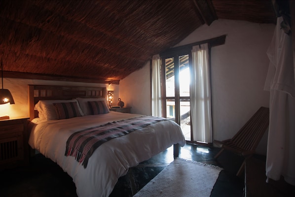 A bedroom with a large bed, wooden headboard, and a nightstand with a lamp. There is a window with curtains and a view of the outside. - casa gaiolas (Ubatuba)