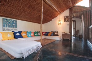 A spacious room with a high ceiling, a large bed with colorful pillows, a small table, and a wooden bench. - casa gaiolas (Ubatuba)