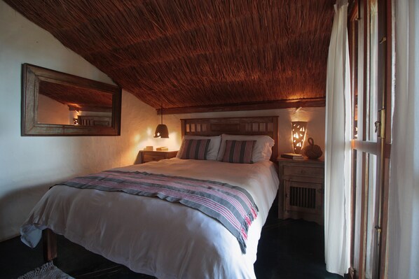 A bedroom with a wooden ceiling, a bed with a striped blanket, bedside lamps, and a nightstand with a lamp.