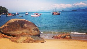 A beach with large rocks in the foreground and several boats on the water. - casa gaiolas (Ubatuba)