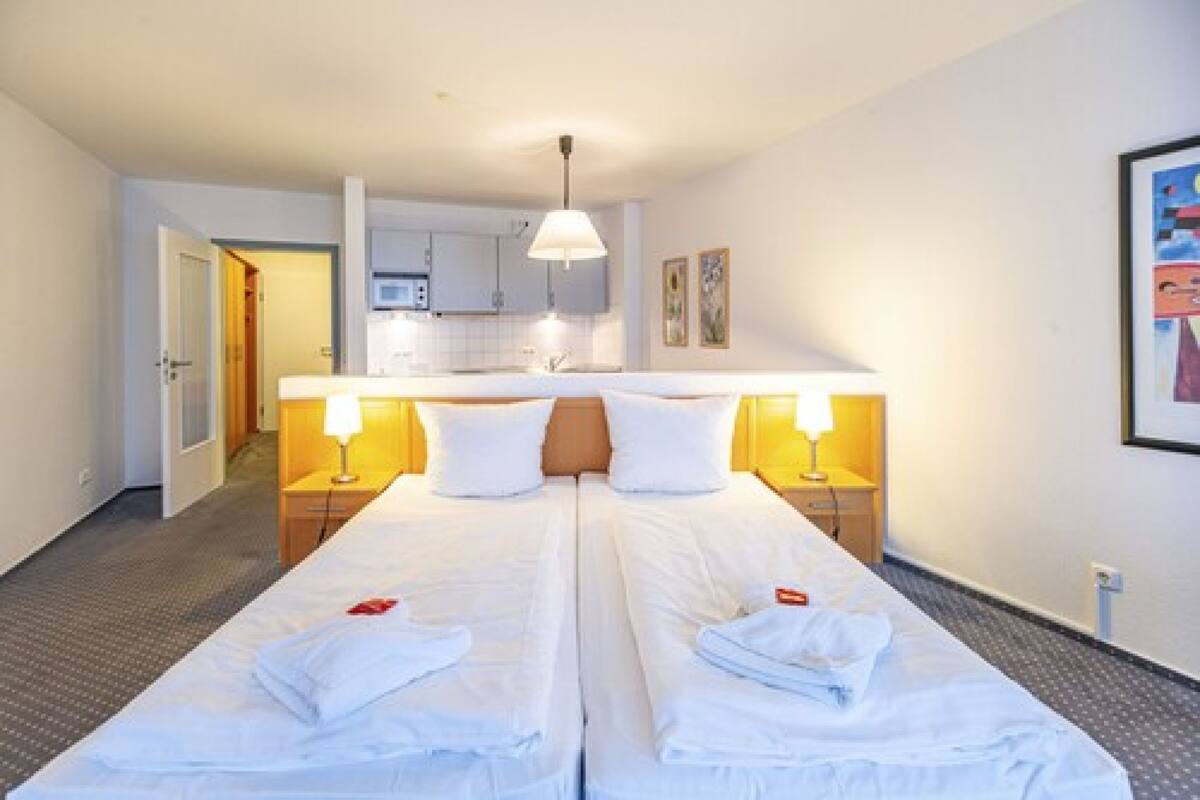 A hotel room with two beds, a kitchenette, and a bathroom visible through an open door.