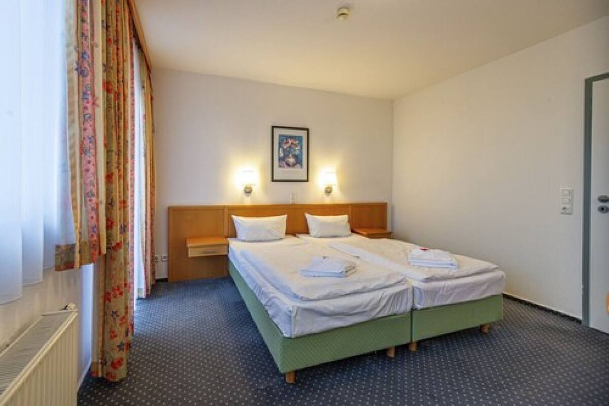 A double bed with two pillows, a nightstand, a framed picture on the wall, and a window with curtains.