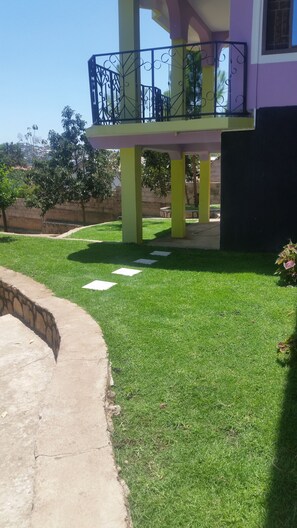 A house with a balcony, a well-maintained lawn, and a stone pathway. - VOT Hostel (Mwanza)