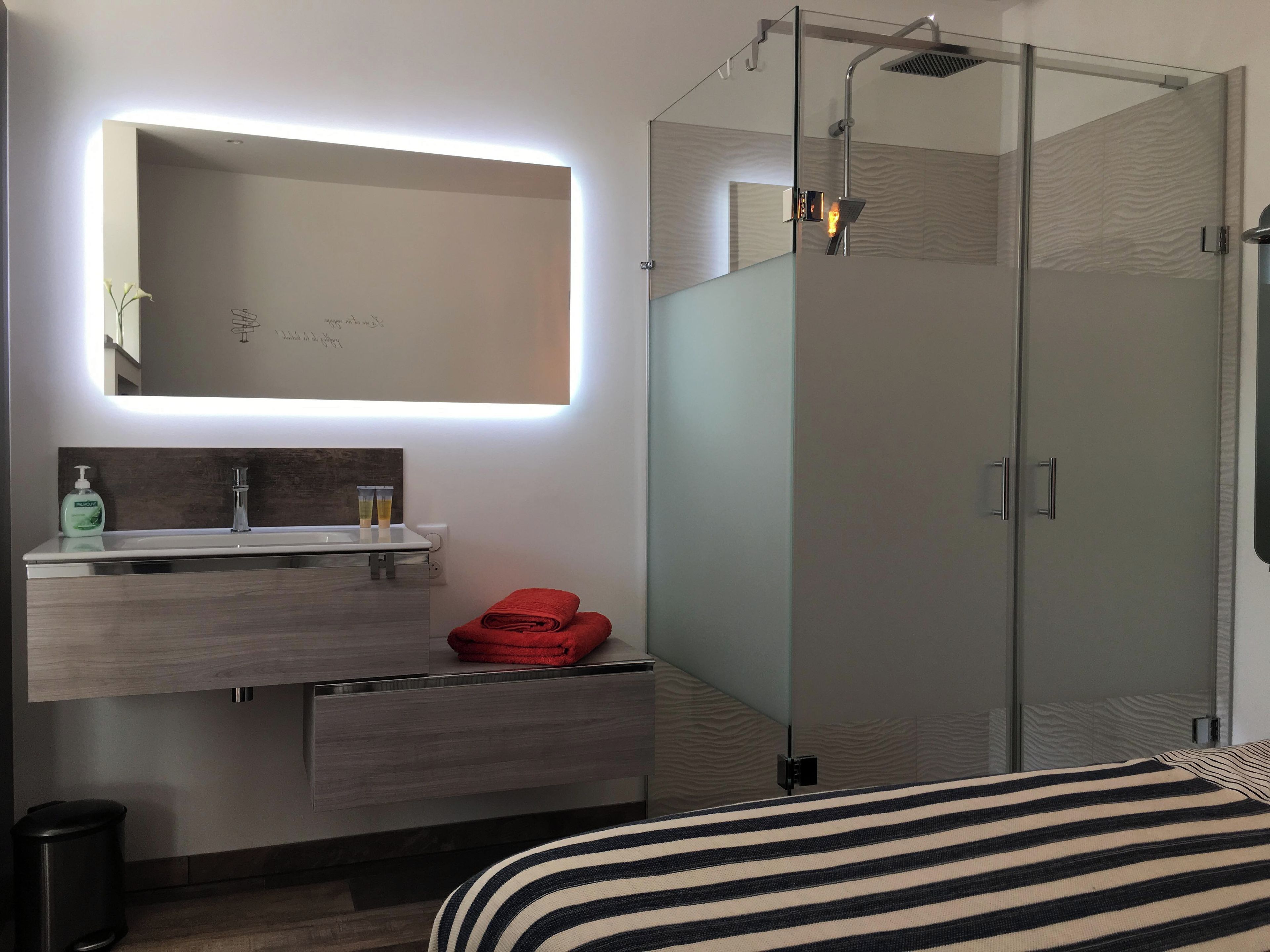 Un baño moderno con cabina de ducha de vidrio, tocador con espejo y cama con ropa de cama a rayas.