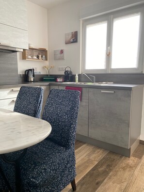 Cocina compacta con comedor, que incluye una mesa de mármol, sillas estampadas y una ventana con luz natural.