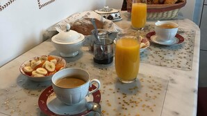 Une table de petit-déjeuner avec des croissants, du jus d’orange, du café et un saladier de fruits.