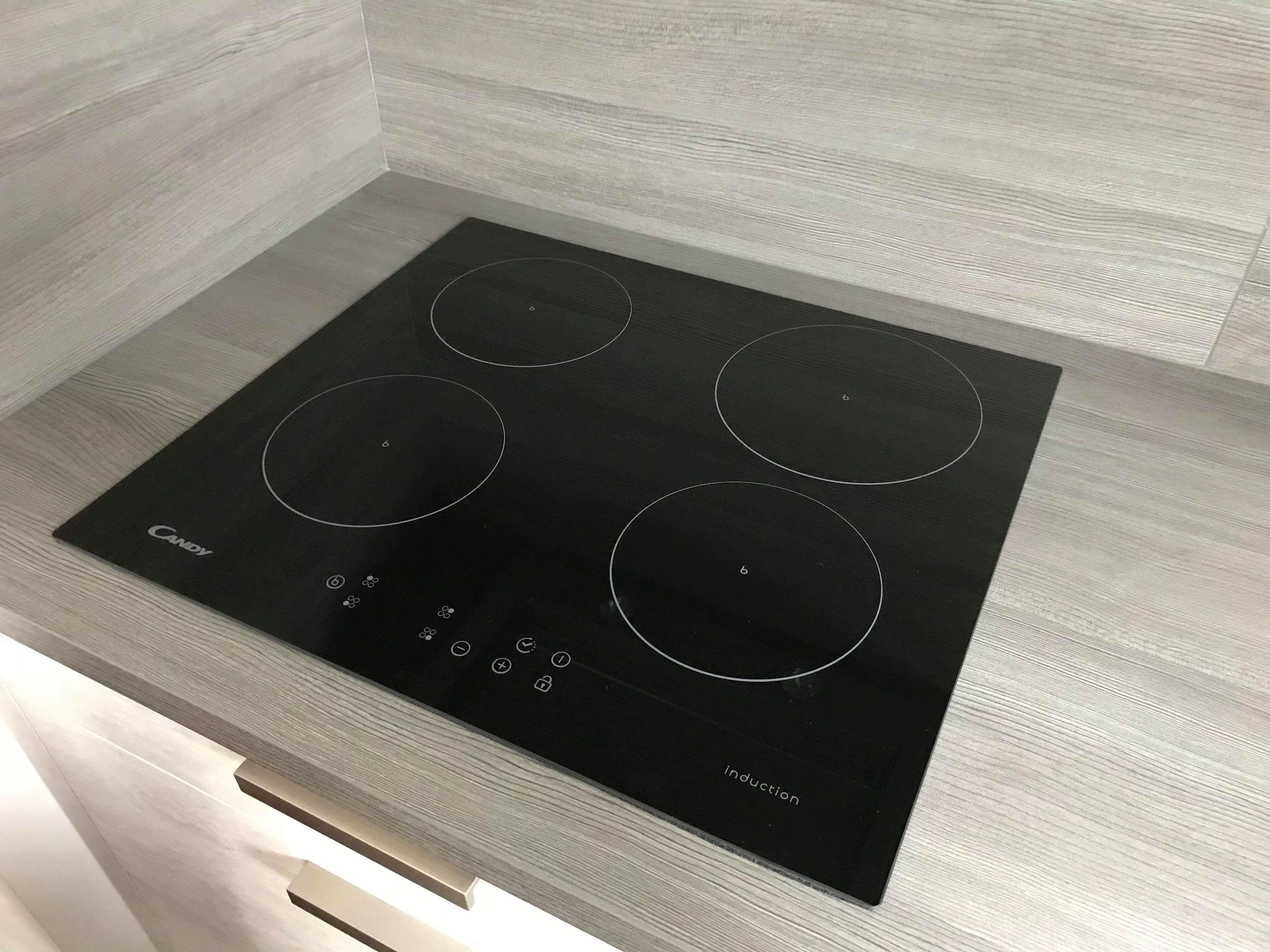 A black induction cooktop with four burners and a control panel with various buttons and a display.