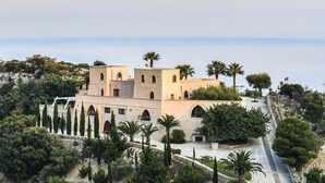 Ein Gebäude im mediterranen Stil mit Bogenfenstern und einem zentralen Innenhof, der von Palmen und Zypressen umgeben ist.
