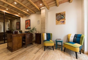 Un hall d’entrée avec un plancher en bois, un comptoir de réception, deux fauteuils colorés et un tableau accroché au mur.
