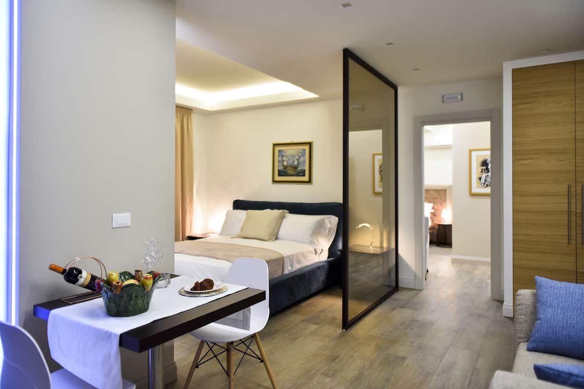Ein modernes Hotelzimmer mit Bett, Esstisch, einer Weinflasche, Stuhl und einer Couch.