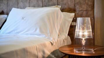 A neatly made bed with white linens and a clear lamp on a wooden bedside table.