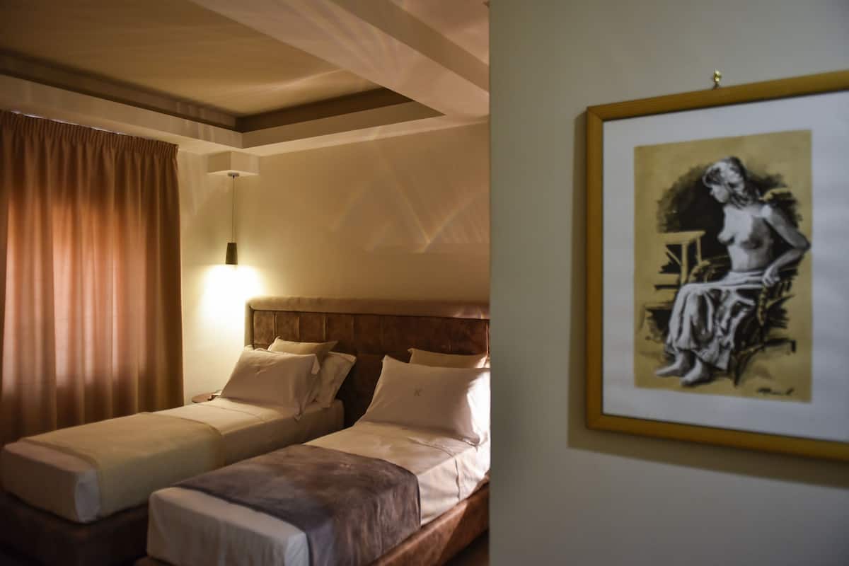 Ein Hotelzimmer mit zwei Betten, einem Kopfteil, einem gerahmten Kunstwerk an der Wand und einem Fenster mit Vorhängen.