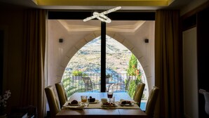 Ein Essbereich mit einem Tisch für vier Personen, einer Chandelierleuchtre und Blick auf eine Berglandschaft durch ein Bogenfenster.