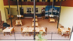 A dining area with multiple tables and chairs, a mural on the wall, and a view of the dining area through a glass partition. - Keys Hotel Mbokomu Branch (Moshi)