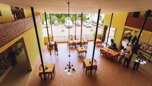 A restaurant with multiple dining tables and chairs, a brick wall on one side, and a view of parked cars outside. - Keys Hotel Mbokomu Branch (Moshi)