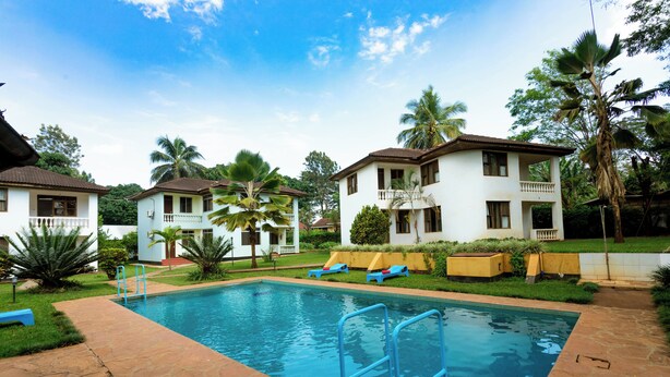 A swimming pool with a stone deck, surrounded by palm trees and a white building with a balcony. - Keys Hotel Mbokomu Branch (Moshi)