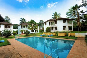 A swimming pool with a stone deck, surrounded by palm trees and a white building with a balcony. - Keys Hotel Mbokomu Branch (Moshi)