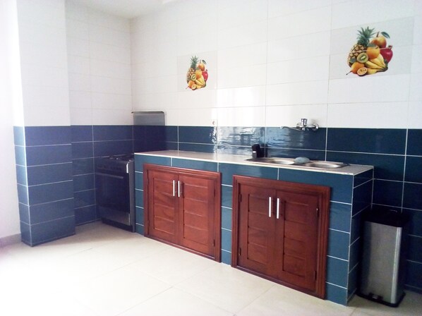Una cocina con baldosas azules y blancas, armarios de madera, un lavamanos de acero inoxidable y un cubo de basura.