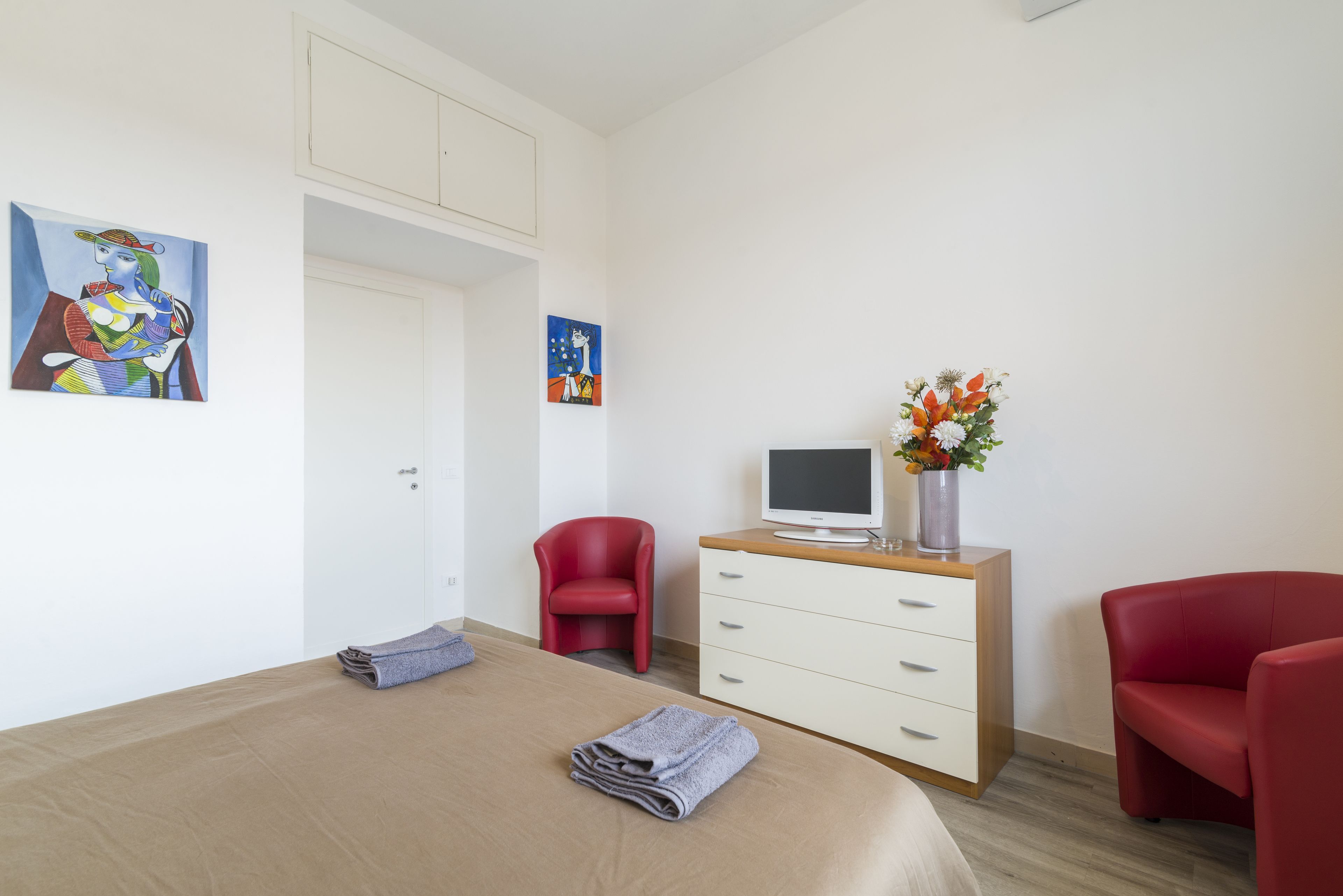 Ein Hotelzimmer mit einem Bett, einem Schreibtisch mit Computer, einem roten Sessel und Bildern an der Wand.