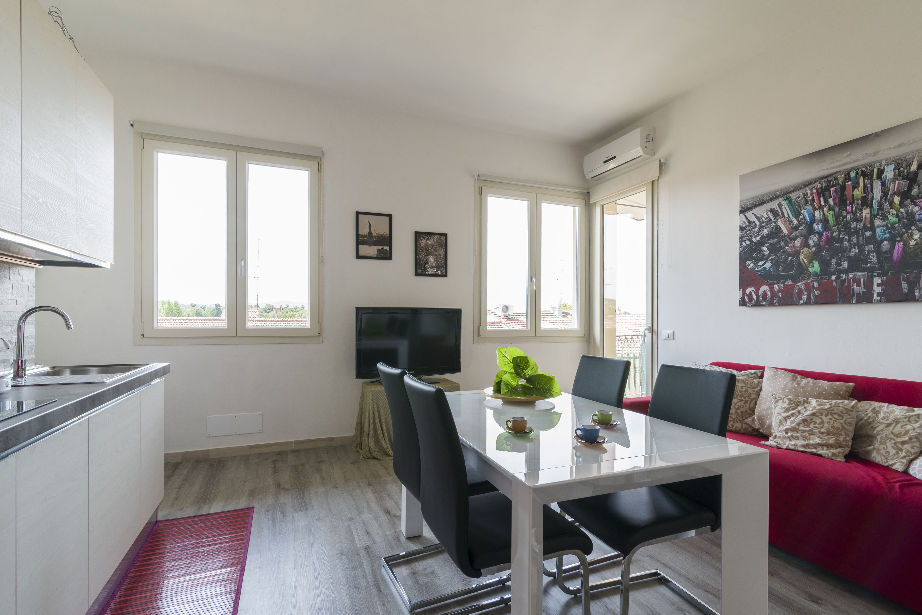 Une cuisine moderne avec un coin repas, un canapé rouge et un téléviseur posé sur un meuble.