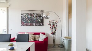 A modern living room with a red sofa, a glass coffee table, a floor lamp, and a cityscape painting on the wall. - Visarno Arena Apartment (Florence)