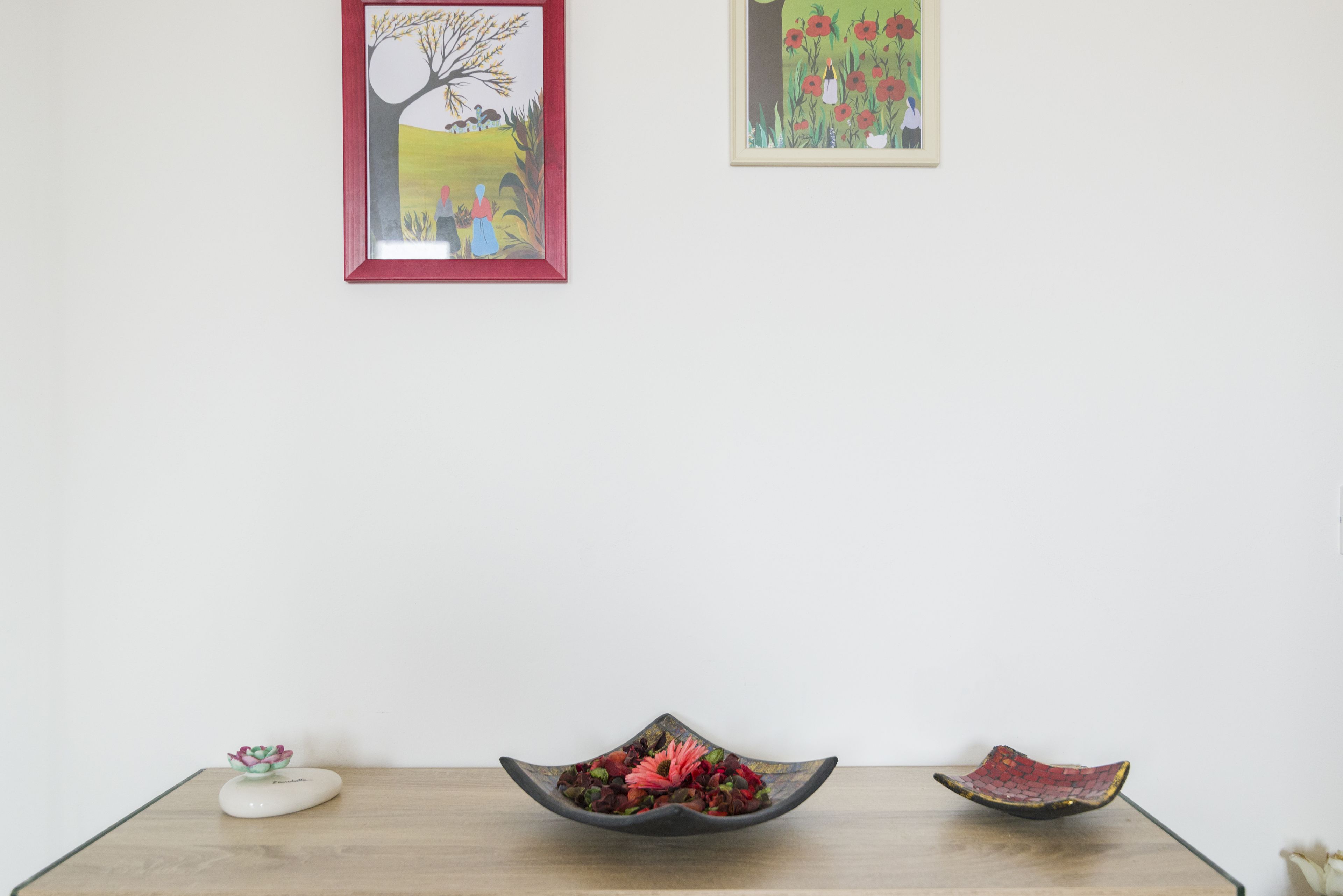 A room with a wooden table, a decorative bowl with flowers, and two framed artworks on the wall.