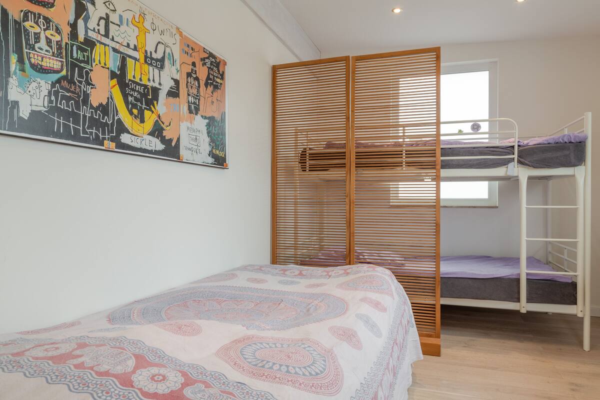 Una habitación con literas, un cuadro abstracto grande y una ventana con persianas.