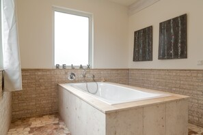 A bathroom with a bathtub, a window, and two abstract paintings on the wall. - Guesthouse Loft (Meerbusch)