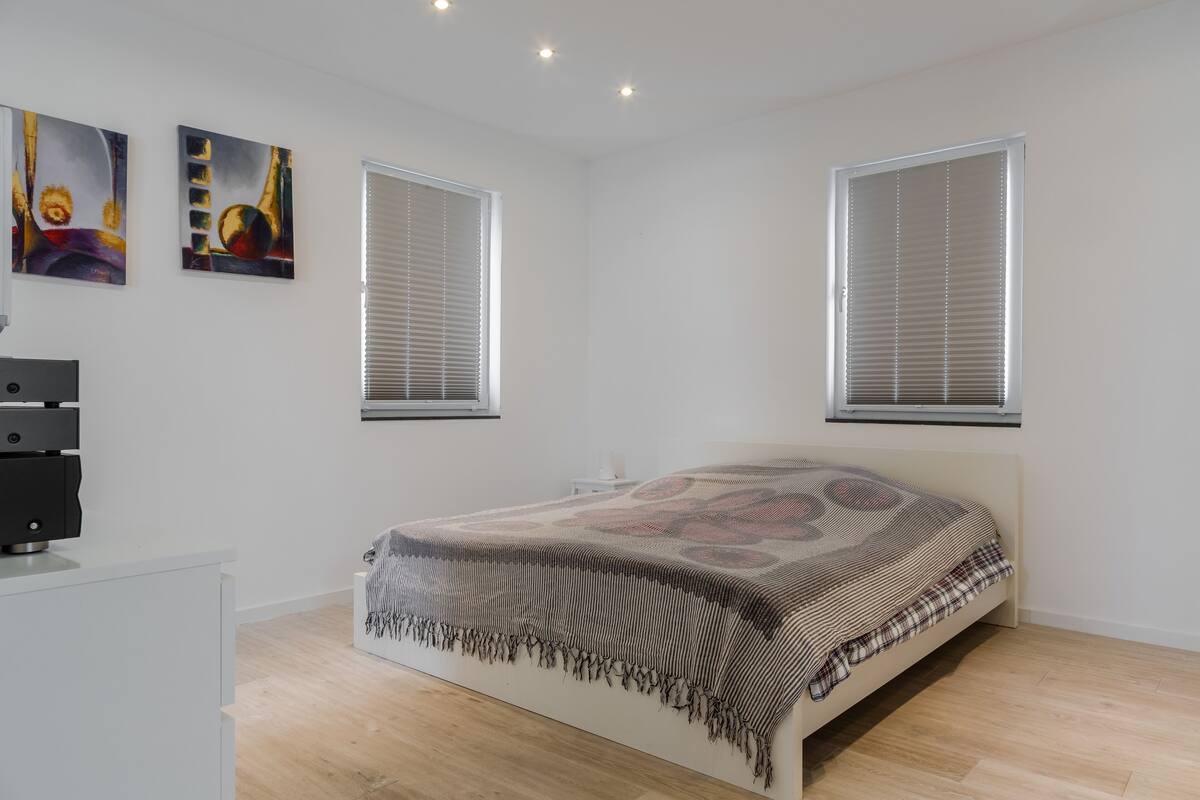 Un dormitorio moderno con cama, dos ventanas y una obra de arte en la pared.