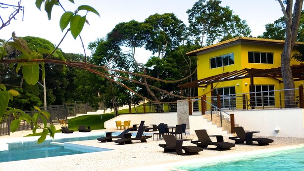 A pool area with lounge chairs and a yellow building in the background. - Casa Villa Firenze (Mata de São João)