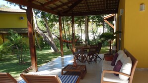 A covered outdoor seating area with wooden furniture, a dining table, and chairs. - Casa Villa Firenze (Mata de São João)
