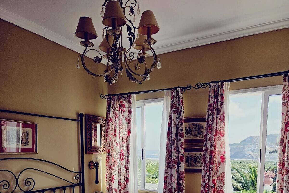 Une chambre d’hôtel avec deux lits, un lustre, des rideaux à motifs floraux et une vue sur le paysage.