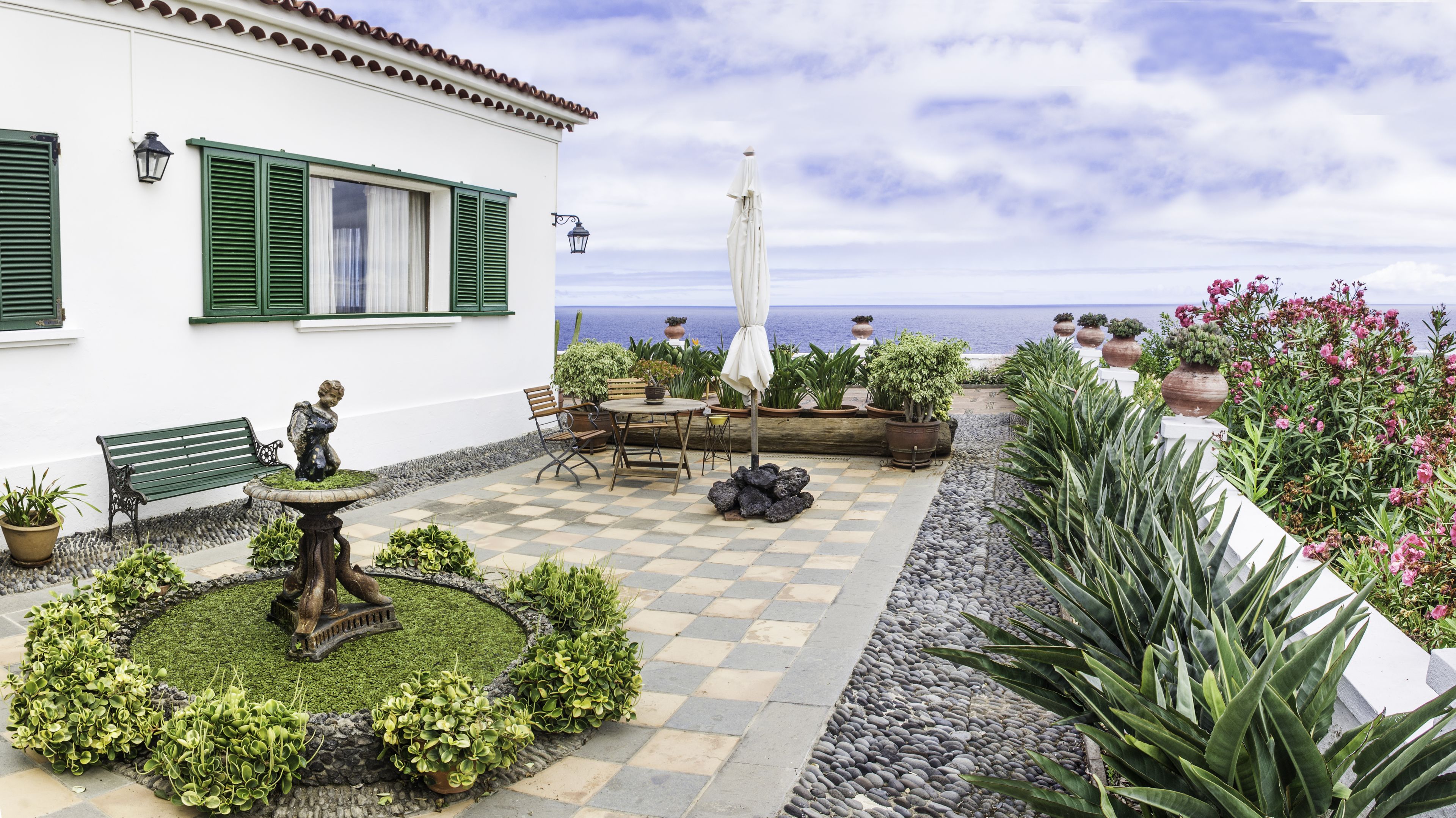 Un patio con suelo a cuadros, mobiliario exterior, plantas en macetas y vista al mar.
