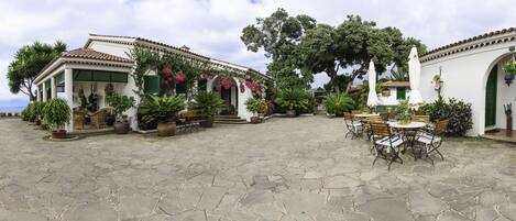 A courtyard with stone flooring, outdoor seating, and potted plants.