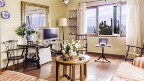 Een woonkamer met een televisie, een tafel met een bloevas, een stoel en een raam met uitzicht op een cactus.