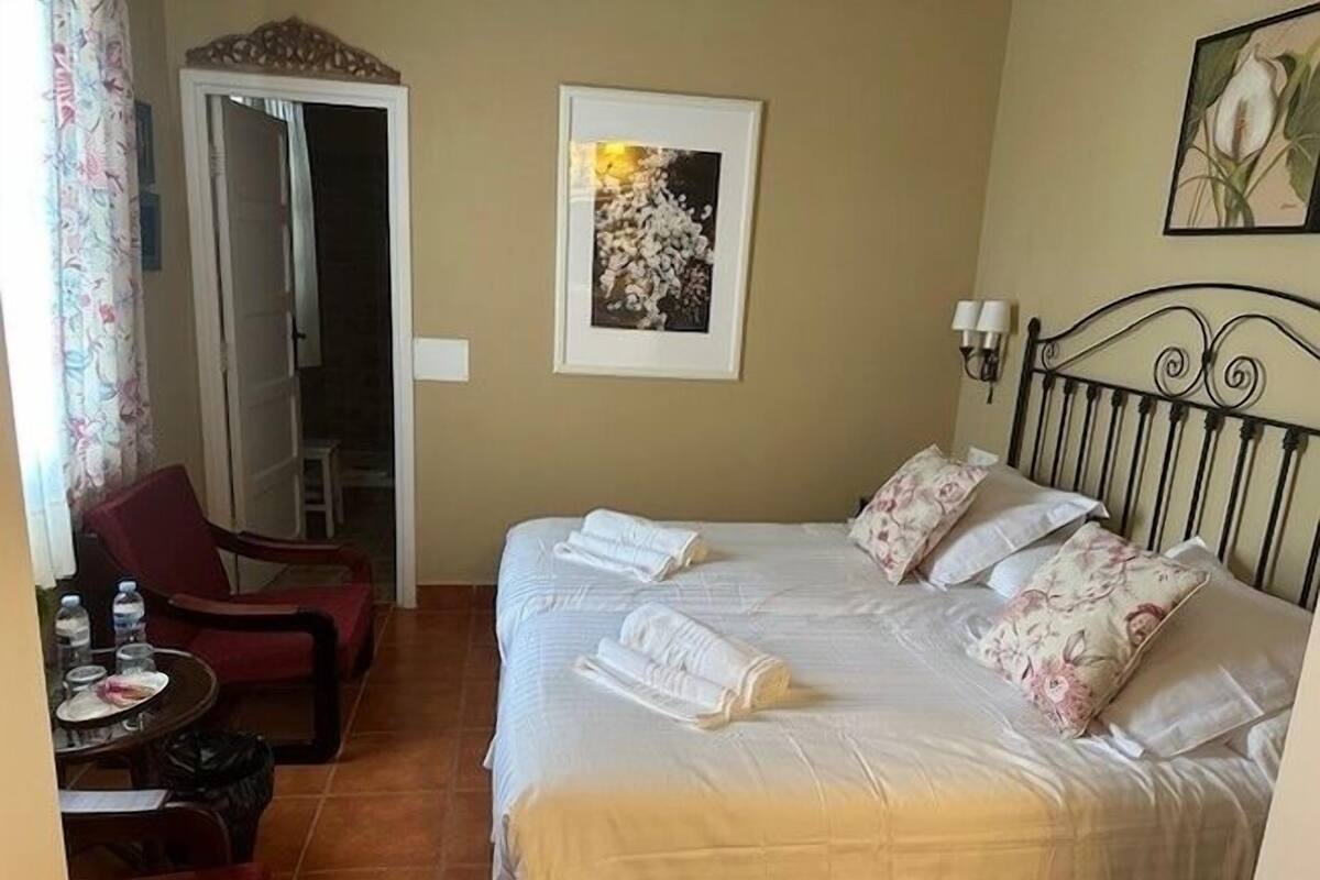 Une chambre d’hôtel avec un lit, une chaise, une table avec des bouteilles d’eau et une porte.